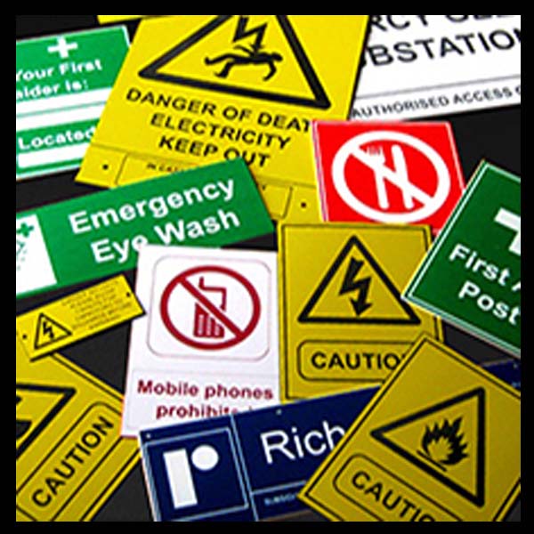 Various industrial lamacoid signs laying on top of eachother, showing the various messages that are engraved on them.